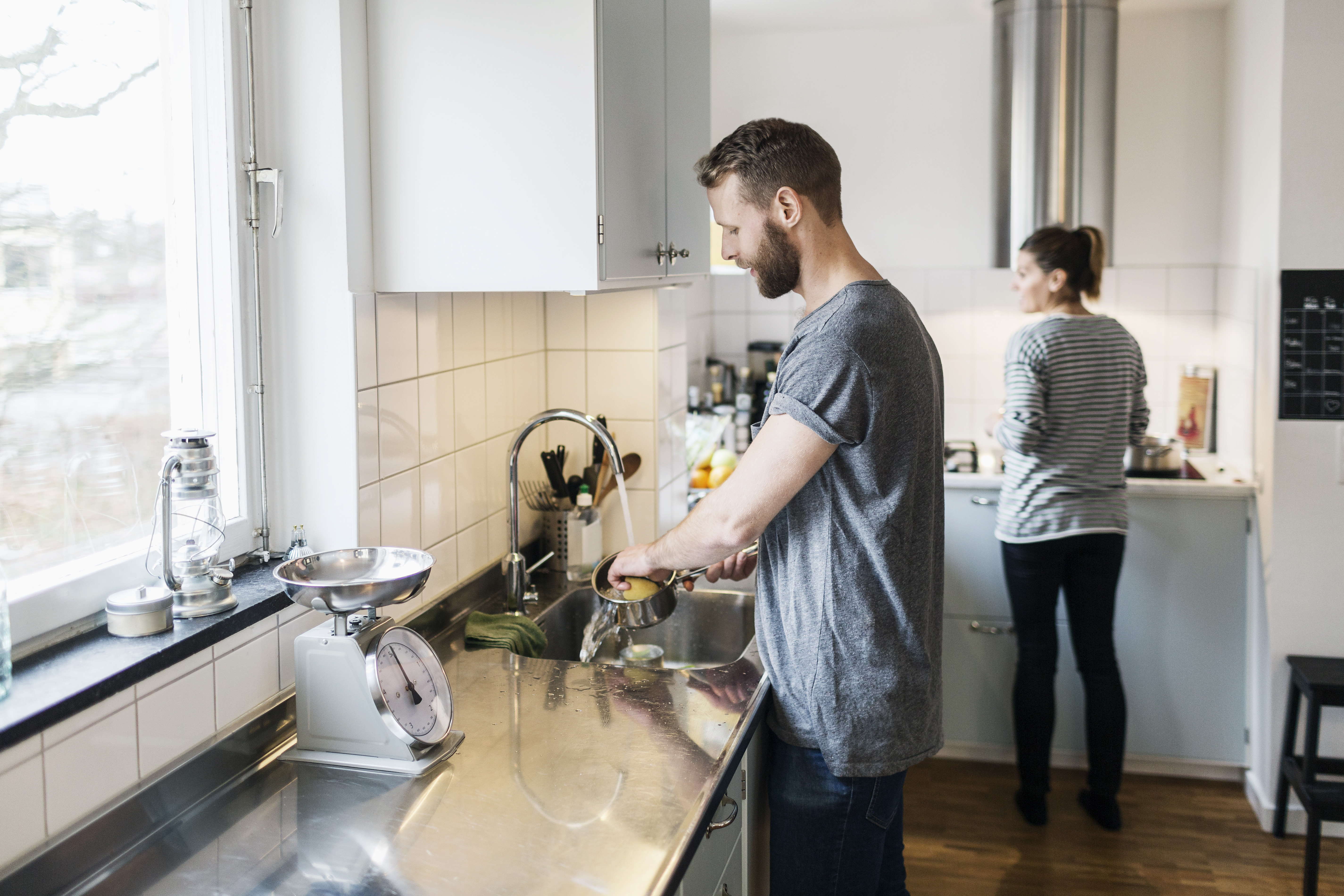 Парень моет посуду. Люди на кухне. Мужчина и домашнее хозяйство. Мужчина по дому. Человек стоит на кухне.